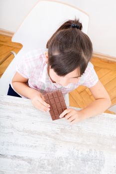 Girl eating chocolate at the table at home while the mother is working.
