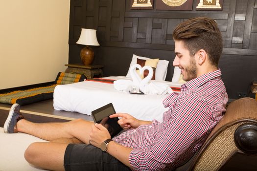 A young man using a tablet pc in a asian hotel room.	