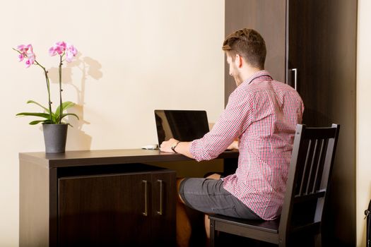 A young and handsome man using a laptop computer in a asian styled hotel room.
