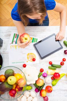 A young adult woman informing herself with a tablet PC about nutritional values of fruits and vegetables.
