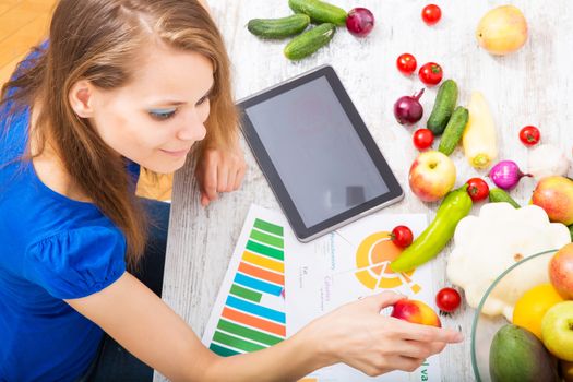 A young adult woman informing herself with a tablet PC about nutritional values of fruits and vegetables.
