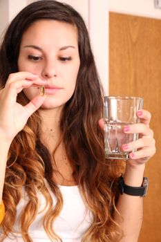 A young woman taking a pill with a glass of water.