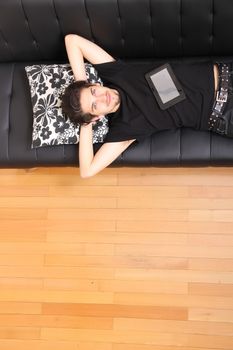 A young hispanic man lying on the sofa holding a Tablet PC.