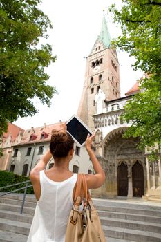 Hispanic girl taking photos of a cathedral with a tablet.

