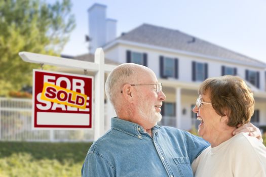 Happy Affectionate Senior Couple Hugging in Front of Sold Real Estate Sign and House.