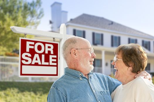 Happy Senior Couple Front of For Sale Real Estate Sign and House.