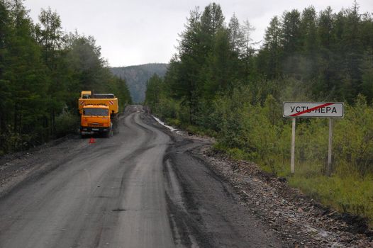 Town name metal plate and truck at gravel road, Kolyma highway, Yakutia, outback of Russia