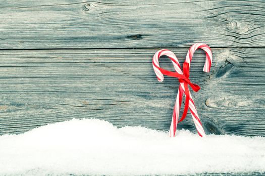 Colorful striped red and white Xmas candy canes with winter snow on wooden boards, with copyspace