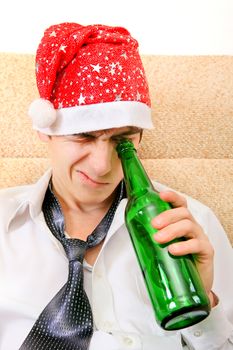 Teenager in Santa Hat looking into the Empty Bottle of the Beer on the Sofa