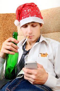 Teenager in Santa Hat with Bottle of the Beer and Cellphone on the Sofa at the Home