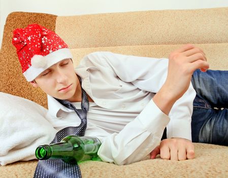 Sad and Tired Teenager with Bottle of the Beer and Santa Hat on the Sofa at the Home