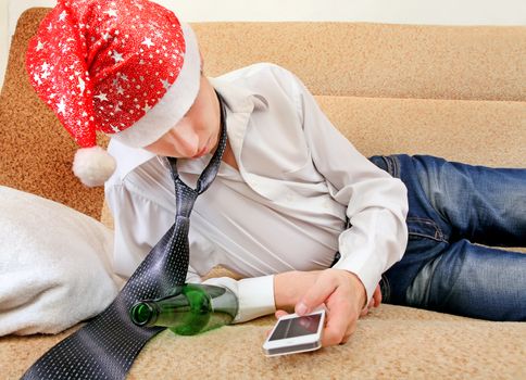 Sad and Tired Teenager in Santa Hat with Bottle of the Beer and Cellphone on the Sofa