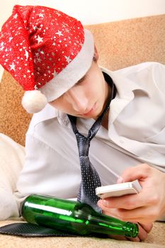 Sad and Tired Teenager in Santa Hat with Bottle of the Beer and Cellphone on the Sofa