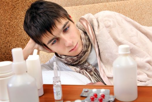 Sad and Sick Teenager on the Sofa at the Home with Pills on foreground