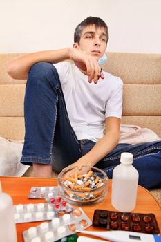 Sick Teenager smoking Cigarette on the Sofa with the Pills on foreground