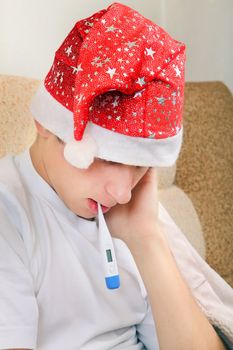 Sick Teenager in Santa Hat with Thermometer on the Sofa at the Home