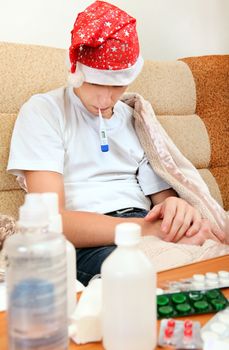 Sick Teenager in Santa Hat with Thermometer on the Sofa with the Pills on the Table