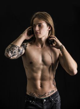 Muscular man shirtless with tattoos, listening to music on headphones isolated on black background