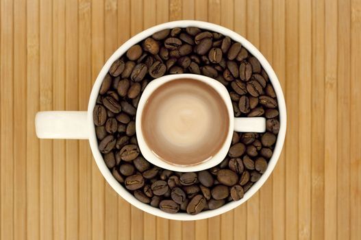 Small cup with espresso inside of big cup, filled with coffee beans