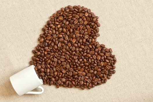 Love shaped coffee beans spilled out of cup of linen fabric