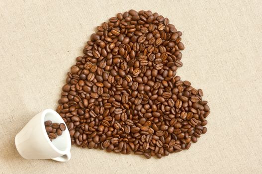 Love shaped coffee beans spilled out of cup of linen fabric