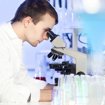 Young male researcher looking at the microscope slide in the life science laboratory. Forensics, microbiology, biochemistry, genetics, oncology...