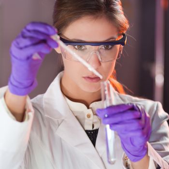 Focused young life science professional pipetting solution into the glass cuvette. Lens focus on the researcher's eye.