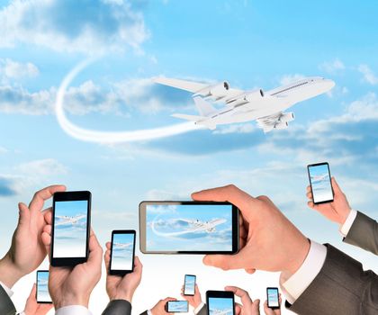 Hands holding smart phones and shoot video as flying airplane. Sky with clouds on background
