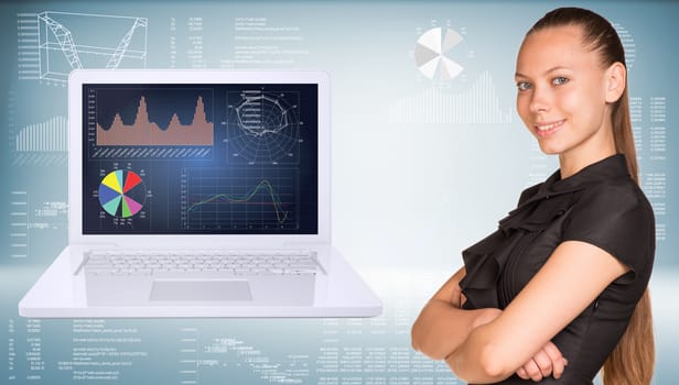 Beautiful businesswoman in dress smiling and looking at camera. Open laptop with graphs on screen are located near. Hi-tech graphs as backdrop