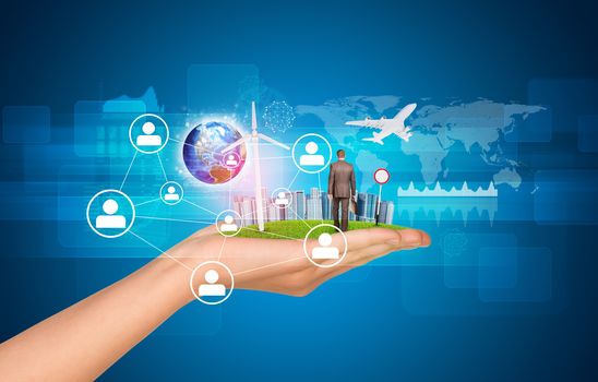 Hand holds city of skyscrapers on green grass and businessman walking forward. Earth and network with people icons near hand. Element of this image furnished by NASA