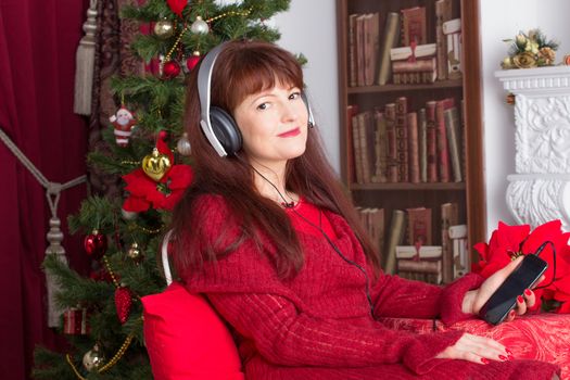Beautiful adult woman listening music against Christmas tree