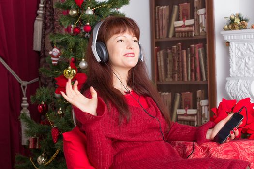 Beautiful adult woman listening music against Christmas tree