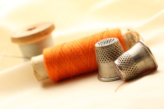 Sewing thimbles, bobbin and needle on silk cloth