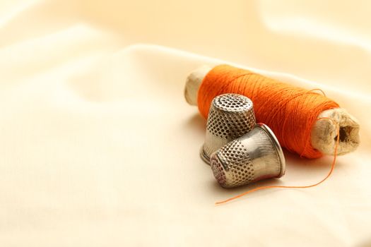 Sewing thimbles, bobbin and needle on silk cloth