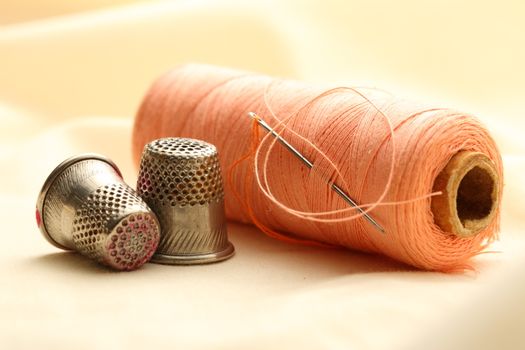 Sewing thimbles, bobbin and needle on silk cloth