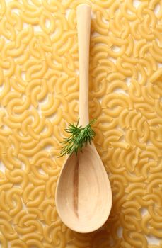 Short ribbed pasta tubes background with spoon and dill