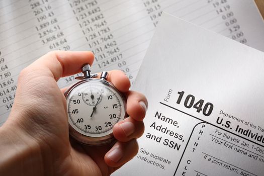 Hand with stopwatch on tax form and budget