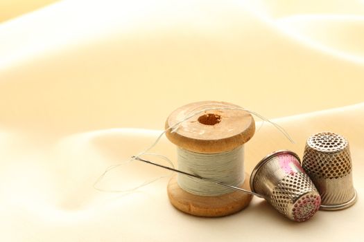 Sewing thimbles, bobbin and needle on silk cloth