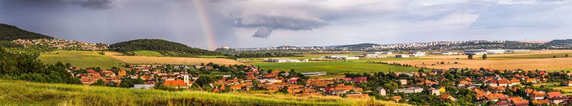 Landscape with Several Populated Areas under Cloudy Sky and Rainbow