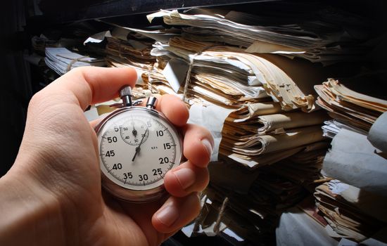 Hand with stopwatch, paper documents stacked in archive