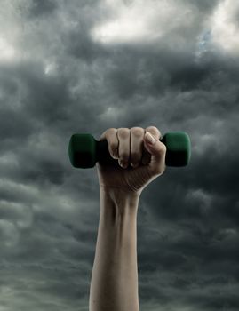 Dumbbell in hand on cloudy sky