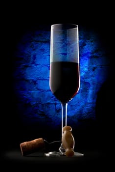 Glass of red wine with corkscrew on wall background