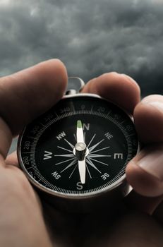 Hand holding black compass on stormy sky background