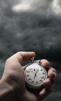 Hand holding stopwatch on stormy sky background