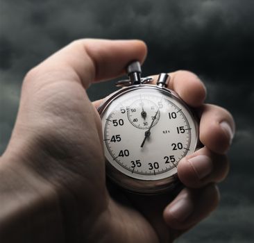 Hand holding stopwatch on stormy sky background