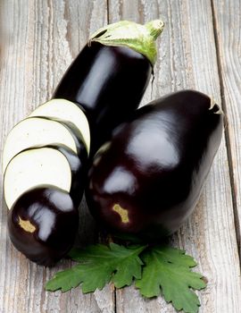 Full Body and Slices of Ripe Raw Eggplants with Leafs isolated on Rustic Wooden background