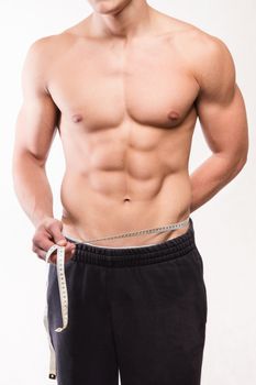 Muscular fitness man measuring his waist - studio shoot 