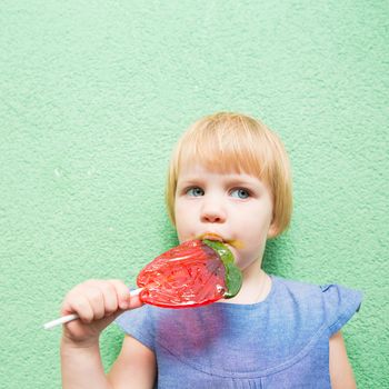 Beautiful little girl holding a big strawberry shaped lollipop