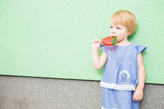 Beautiful little girl holding a big strawberry shaped lollipop