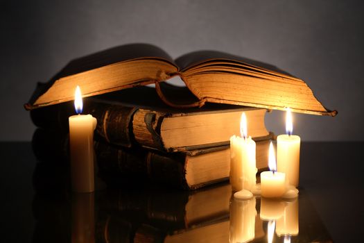 Closeup of stack of old books near lighting candles on dark background